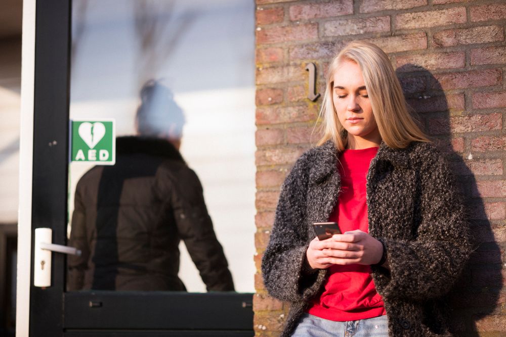 Jonge vrouw staat met haar rug tegen de muur en kijkt op telefoon