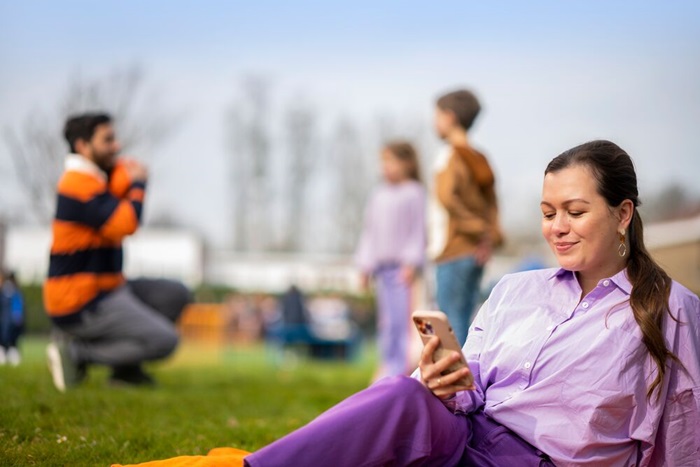 Vrouw kijkt op mobiel gezin speelt in achtergrond