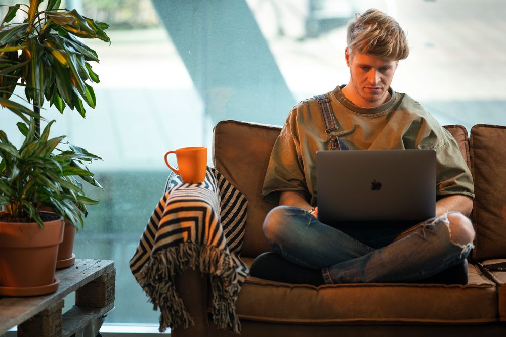 man op bank met laptop en kop thee